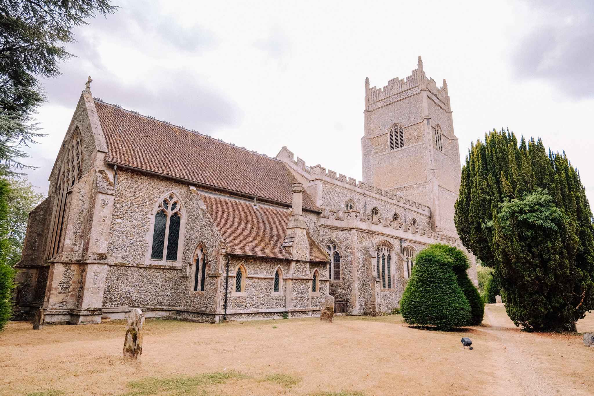 Historic stone church with a tall tower, surrounded by green trees and a grassy area.