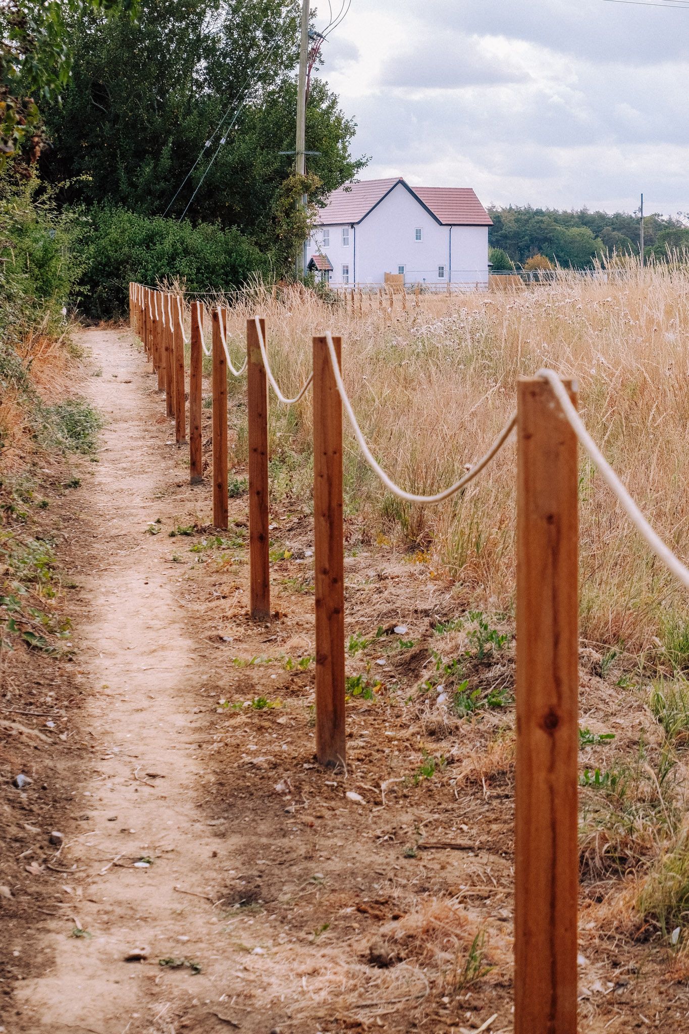 Pathway lined with wooden posts and rope, leading to a white house in a grassy field.
