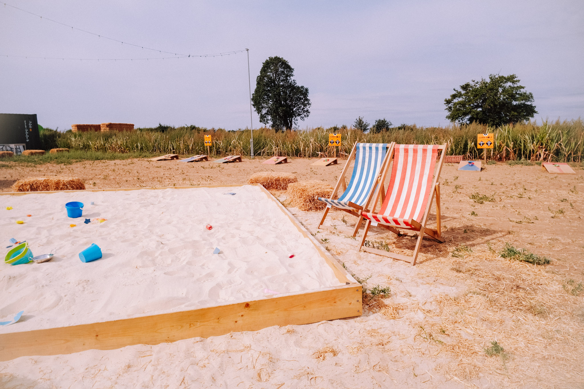 A sandy play area with two striped deck chairs, one blue and white and one red and white, set against a background of grass and signage.