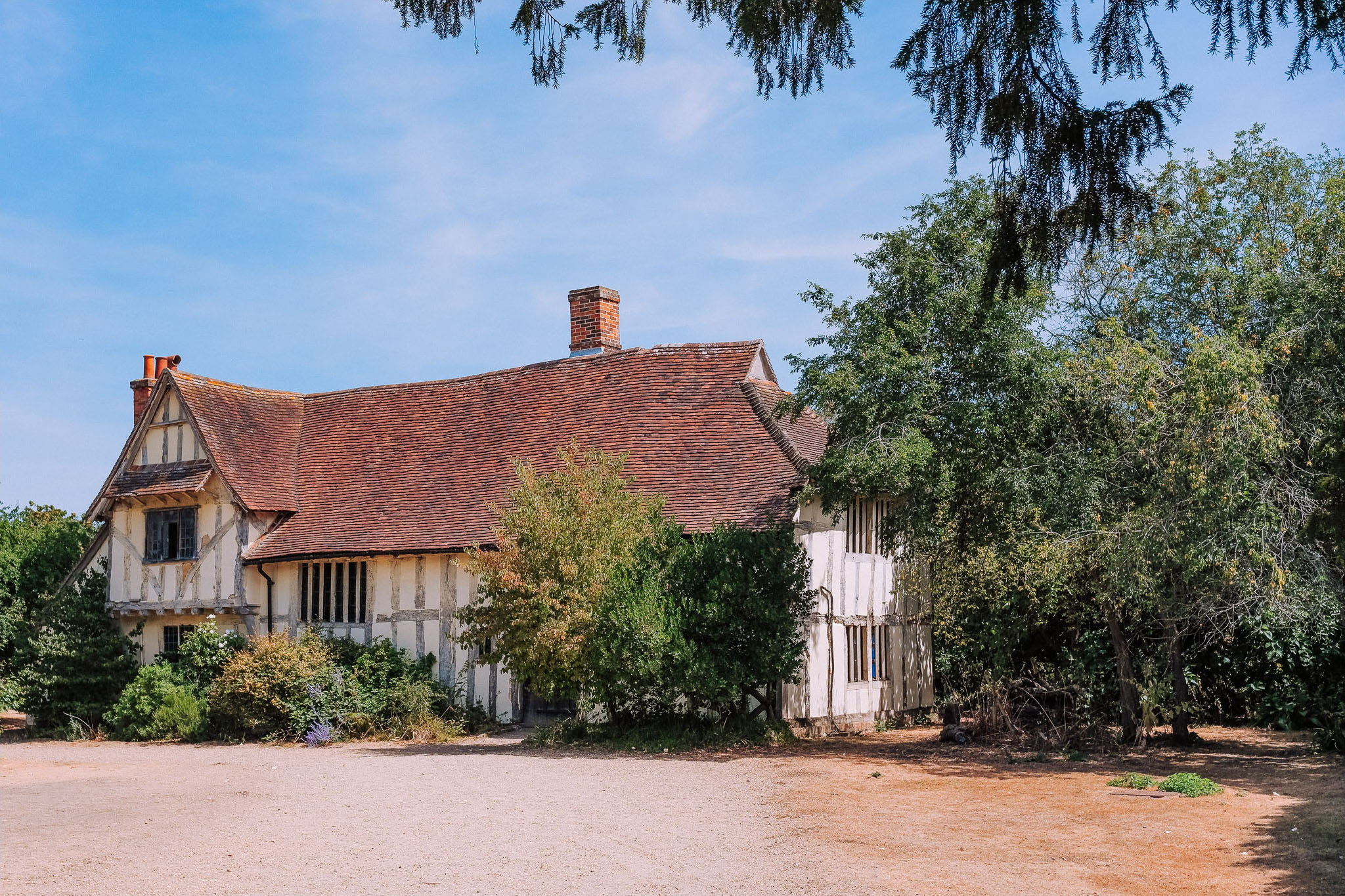 A rustic house with a thatched roof and wooden beams, surrounded by greenery and blue sky.