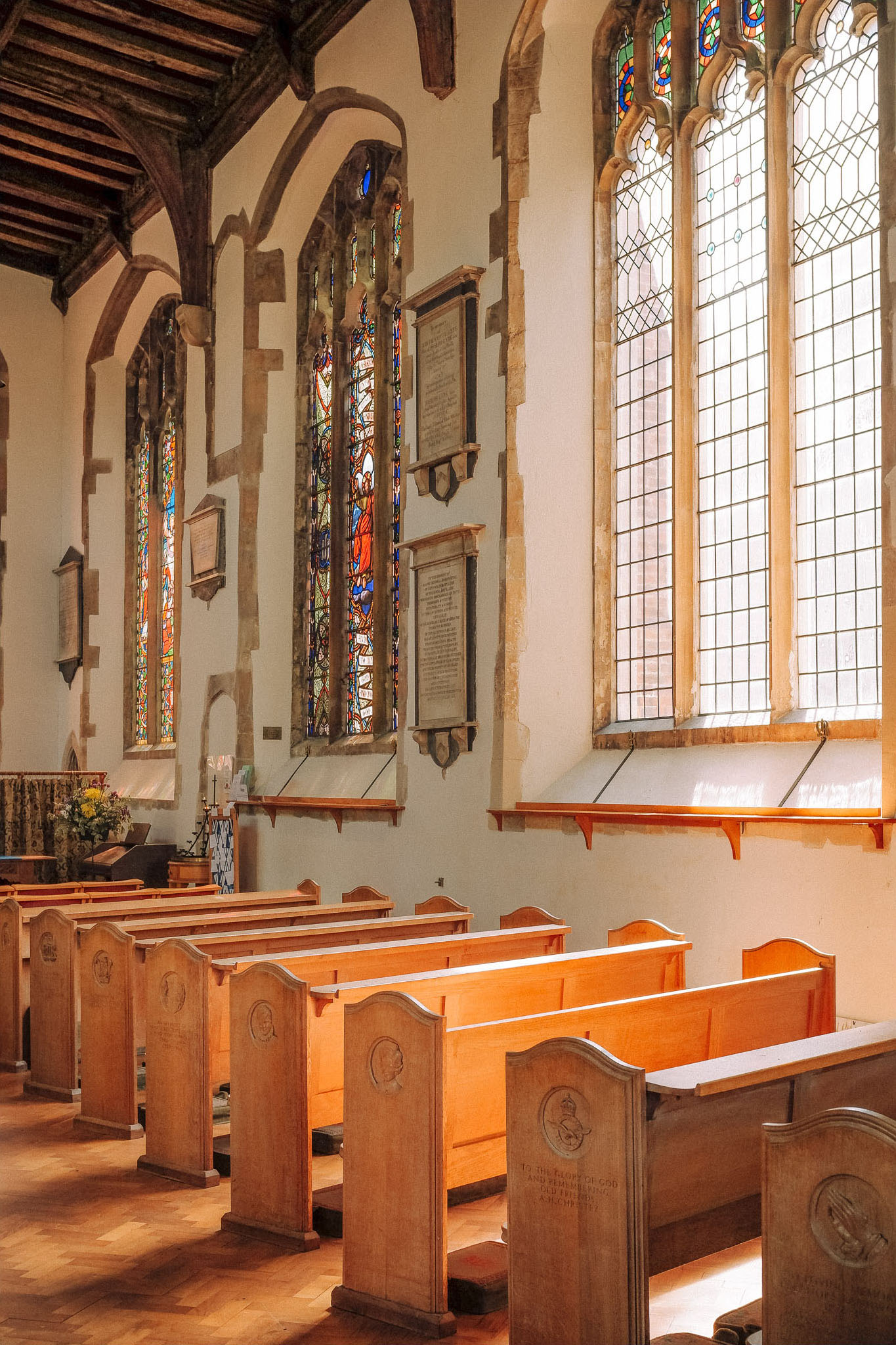 Interior view of a church featuring wooden pews, stained glass windows, and memorial plaques on the walls.
