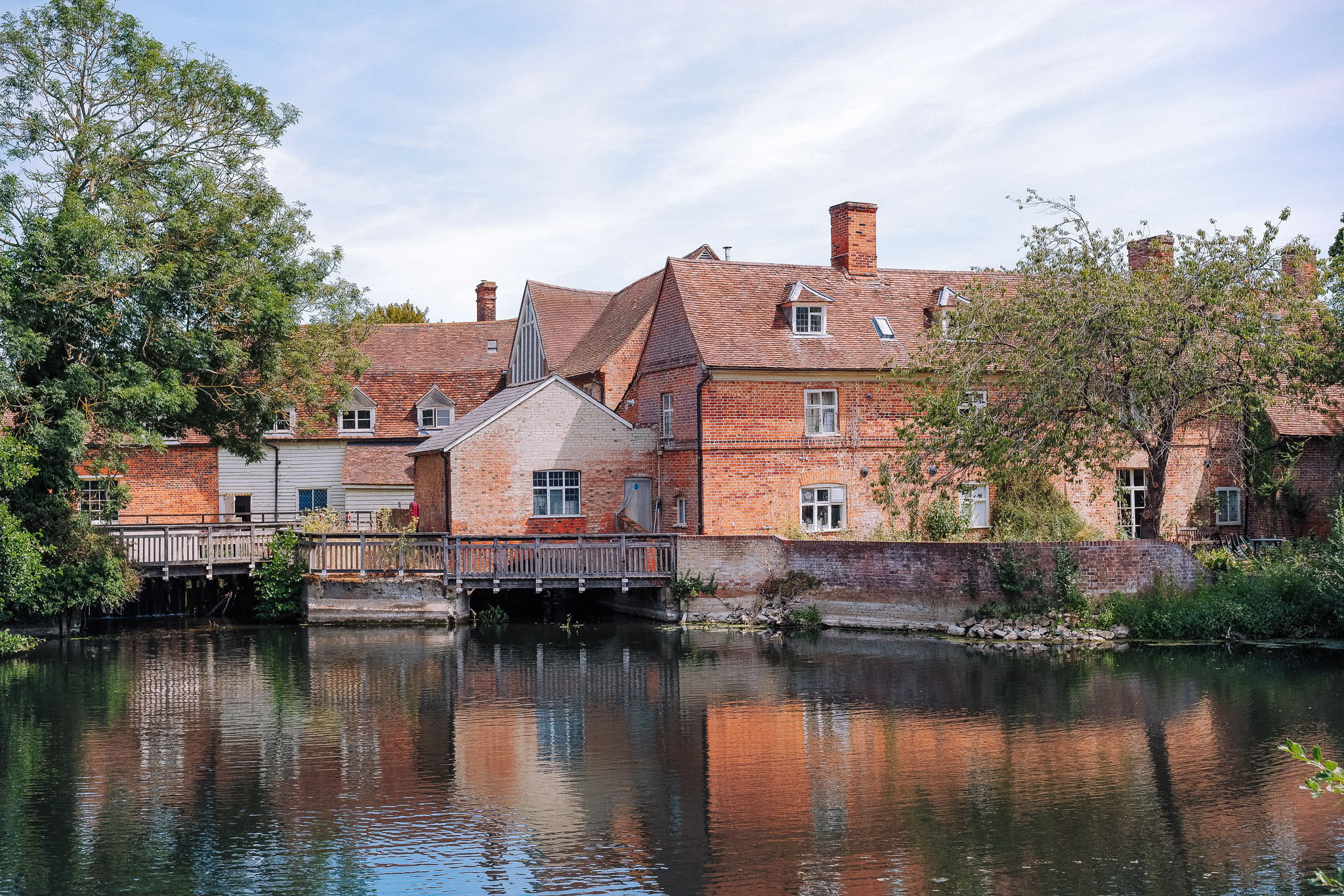 Riverfront view of brick houses with a wooden dock surrounded by trees and reflecting in the water.