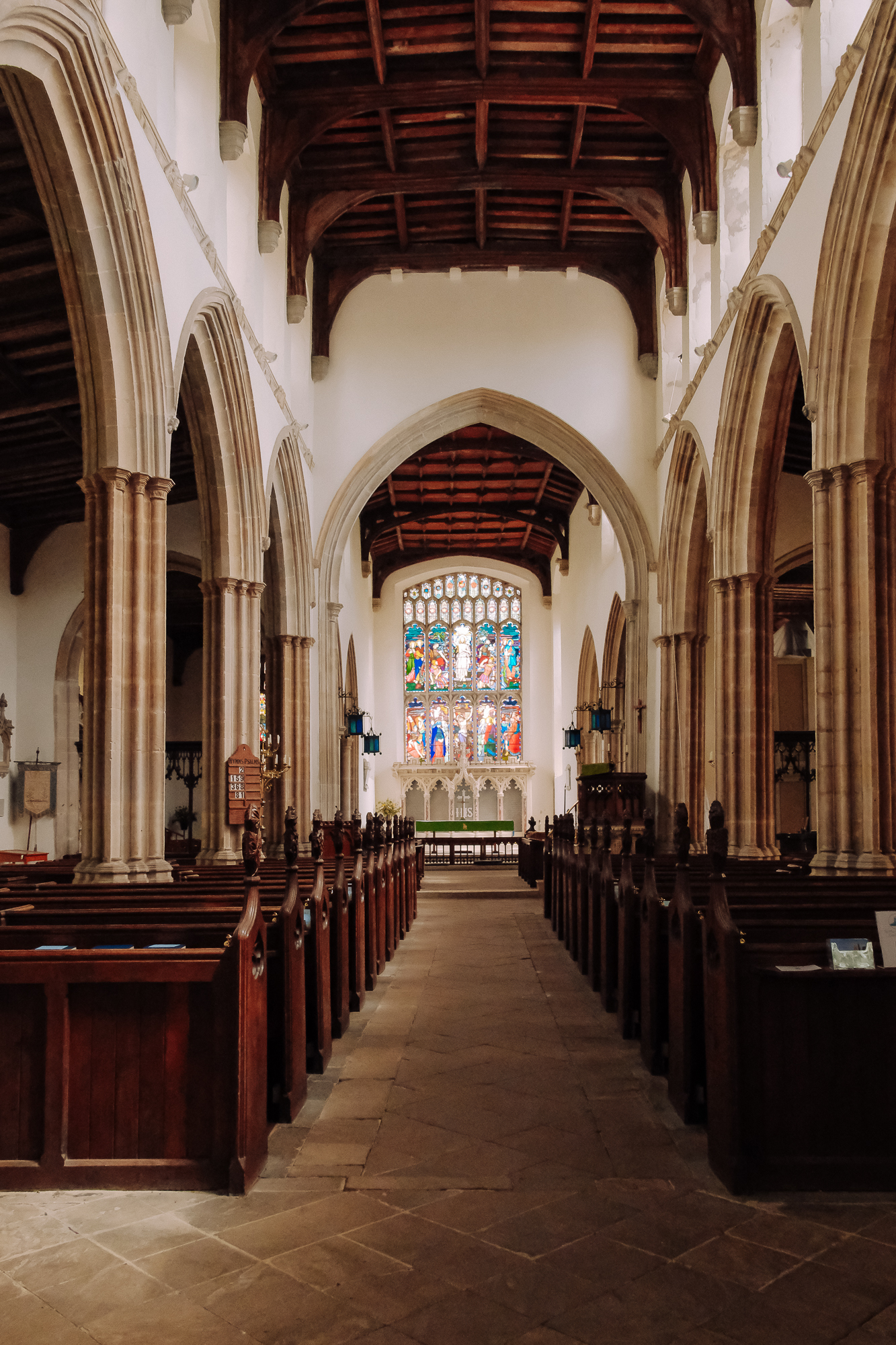 Interior view of a church featuring wooden pews, tall arched ceilings, and a colorful stained glass window at the altar.
