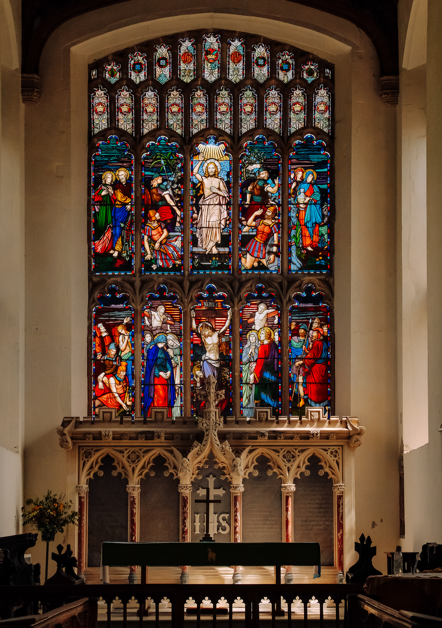 Stained glass window depicting religious figures and scenes, situated in a church, with intricate designs and vibrant colors.